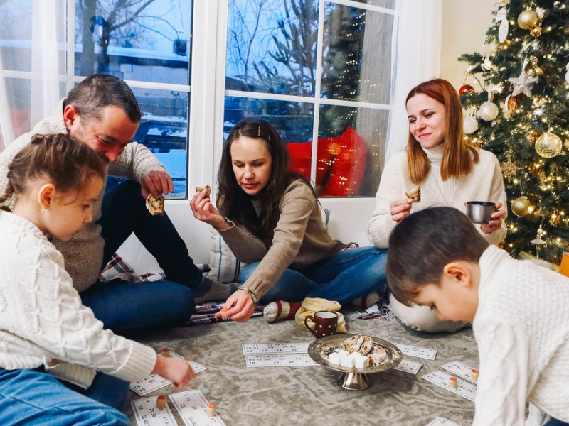 Eine Familie sitzt auf dem Boden vor dem Weihnachtsbaum und spielt ein Gesellschaftsspiel.