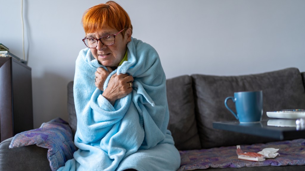 Eine ältere Dame mit roten Haaren ist in eine hellblaue Decke gewickelt.