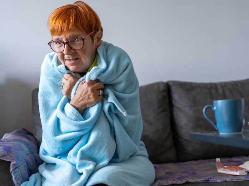 Eine ältere Dame mit roten Haaren ist in eine hellblaue Decke gewickelt.