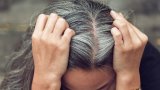 Eine Frau teilt ihren Scheitel und zeigt ihre grauen Haare.