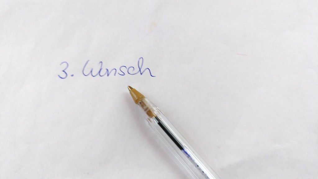 Ein weißes Papier, auf das 3. Wunsch mit einem darauf liegenden Kuli geschrieben wurde.