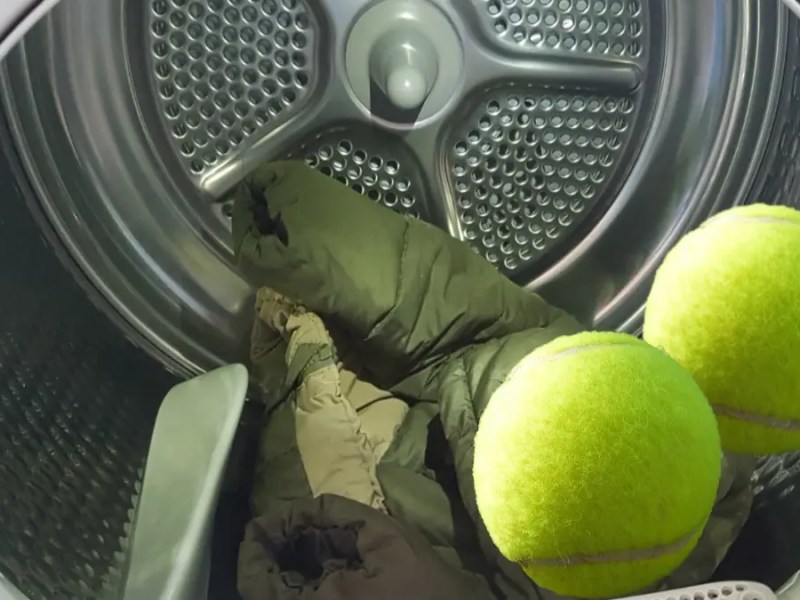 Waschmaschine mit Daunenjacke und zwei Tennisbällen.