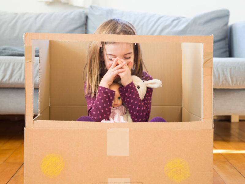 Kind sitzt mit Spielzeug in Kiste