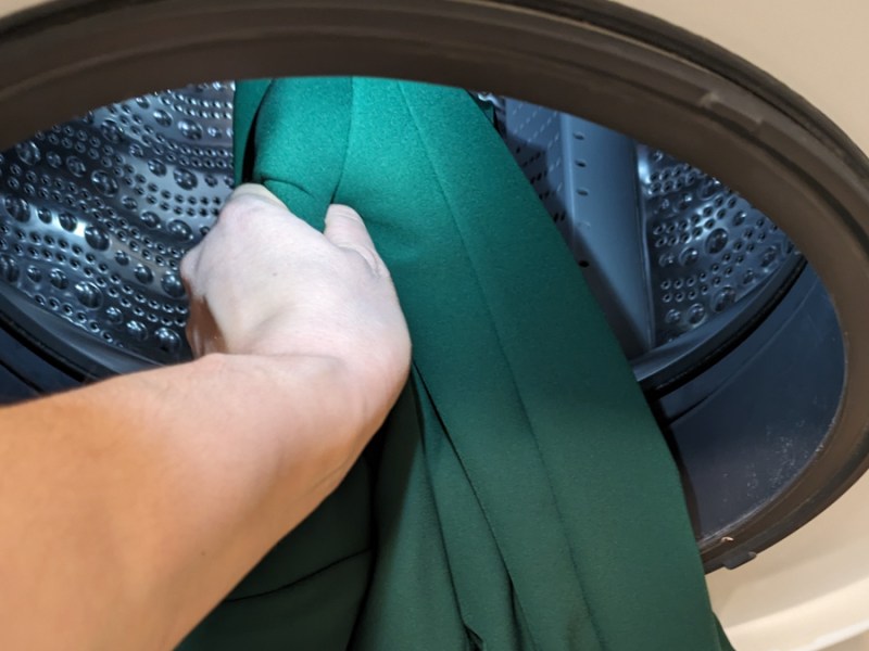 Ein grüner Blazer wird in eine Waschtrommel gelegt.