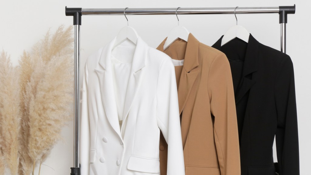 Ein weißer, karamellbrauner und schwarzer Blazer hängen an einer Kleiderstange.