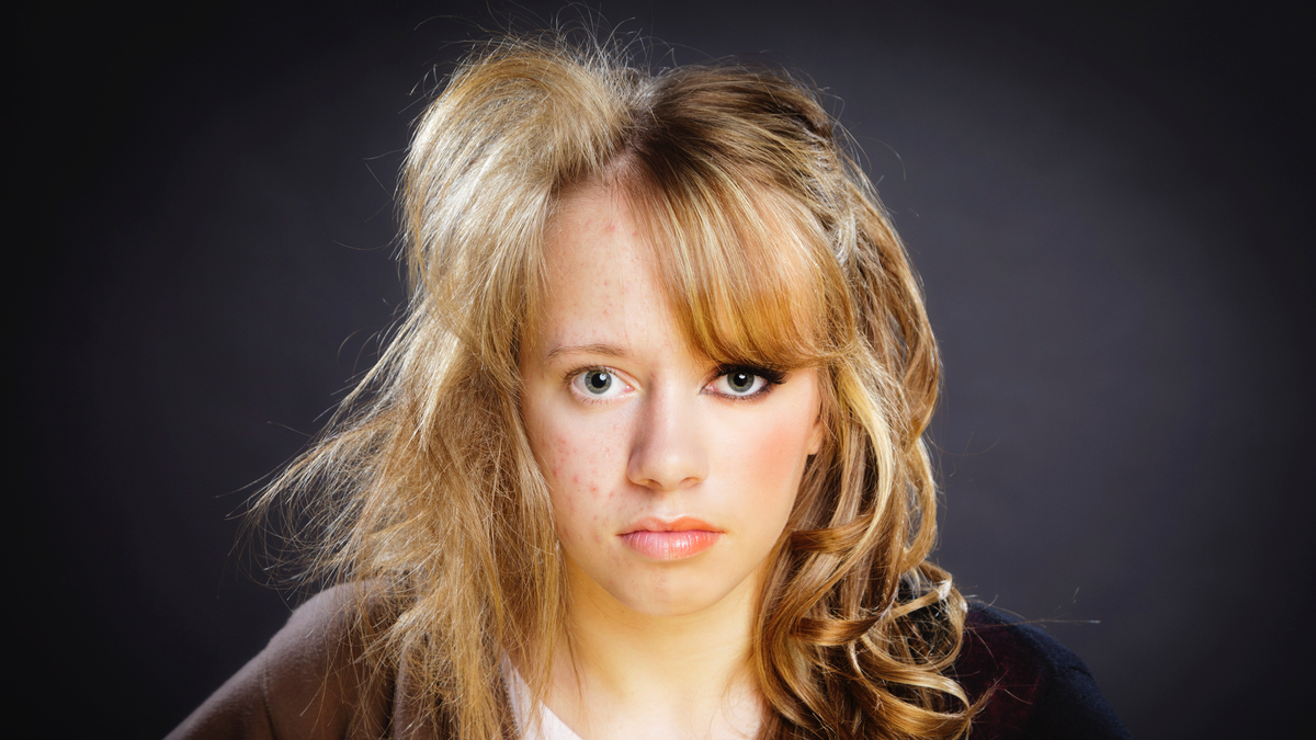 Eine junge Frau mit blonden Haaren ist auf einer Seite des Gesichts geschminkt und gestylt und auf der anderen Seite nicht.
