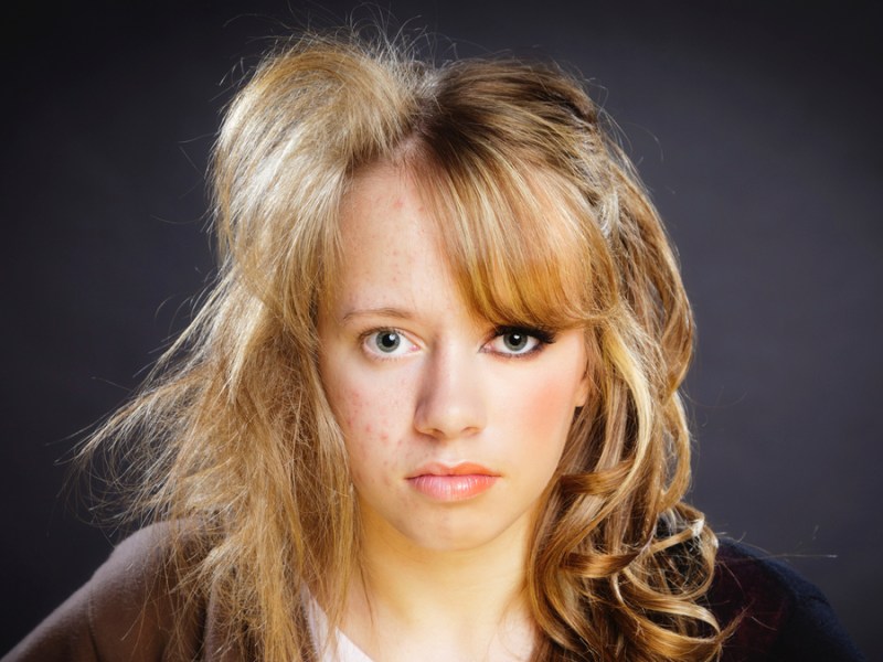Eine junge Frau mit blonden Haaren ist auf einer Seite des Gesichts geschminkt und gestylt und auf der anderen Seite nicht.