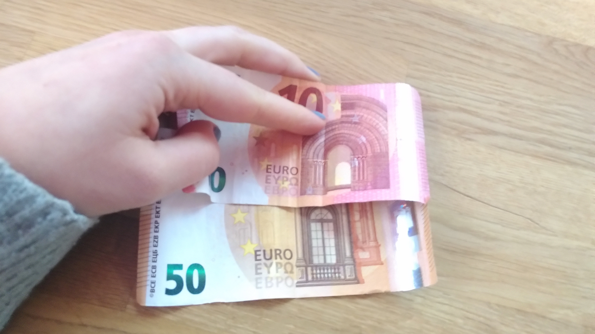Eine Hand hält einen Fünfzig- und Zehn-Euro-Schein auf einen Holztisch.