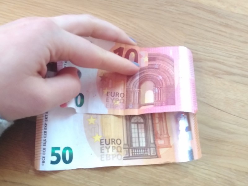 Eine Hand hält einen Fünfzig- und Zehn-Euro-Schein auf einen Holztisch.