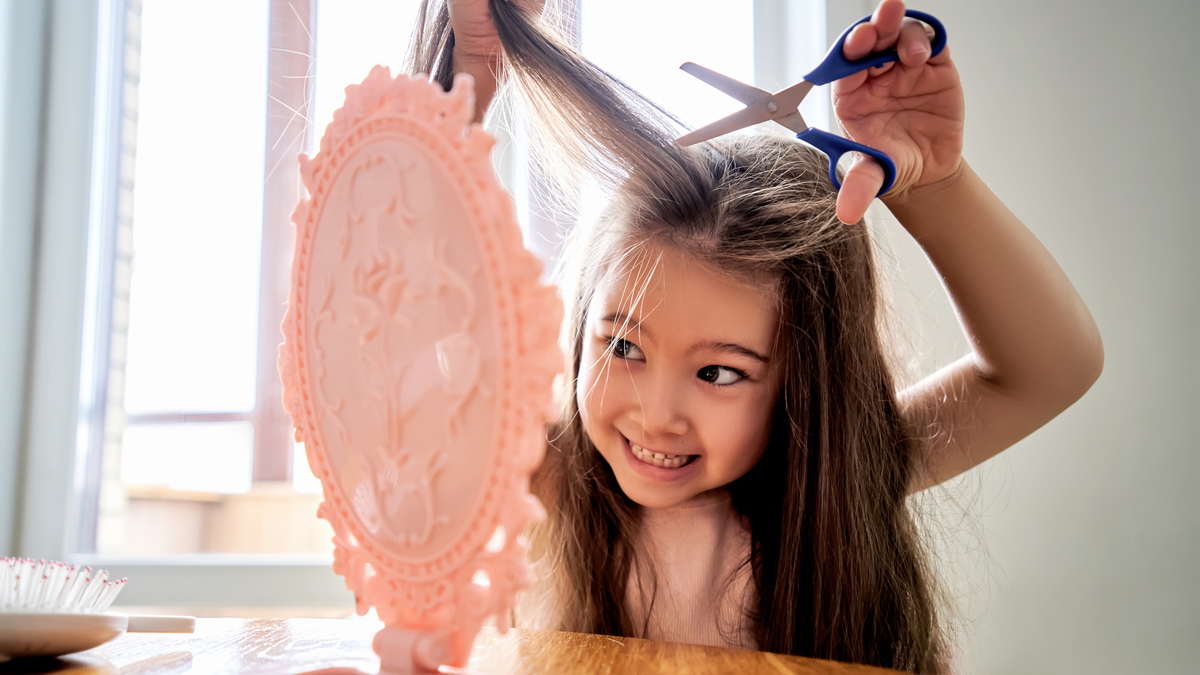 Ein Mädchen versucht vor einem Handspiegel ihre Haare zu schneiden.