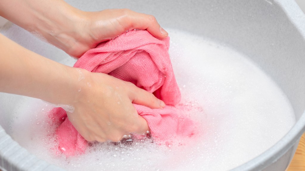 Eine Frau wäscht ein rosa Kleidungsstück mit der Hand.