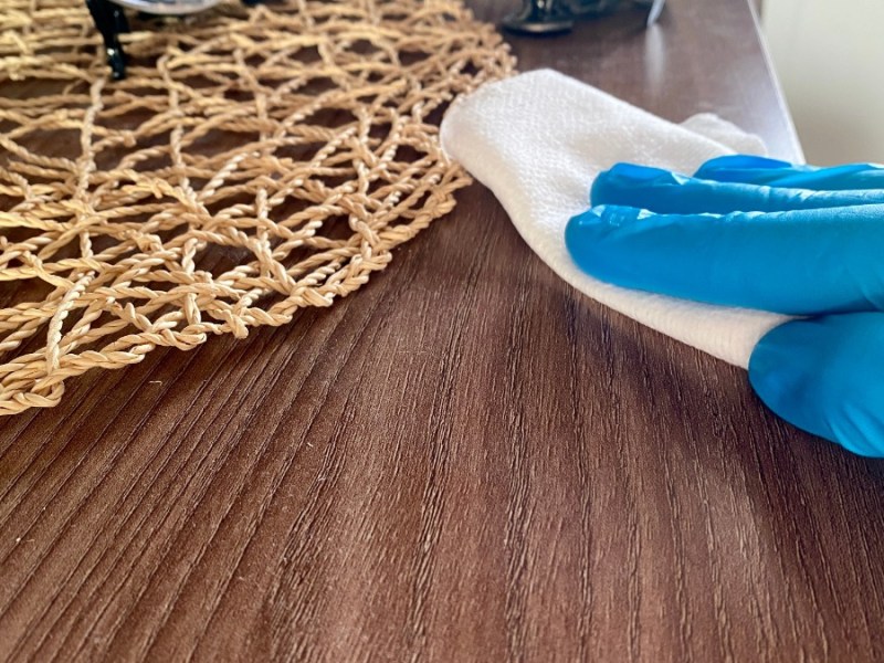 eine Person mit blauen Handschuhen wischt mit einem weißen Tuch über ein Möbelstück