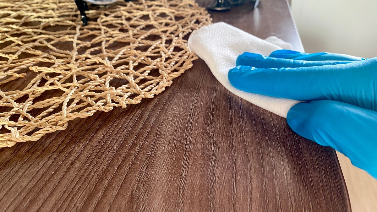 eine Person mit blauen Handschuhen wischt mit einem weißen Tuch über ein Möbelstück