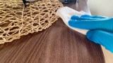 eine Person mit blauen Handschuhen wischt mit einem weißen Tuch über ein Möbelstück