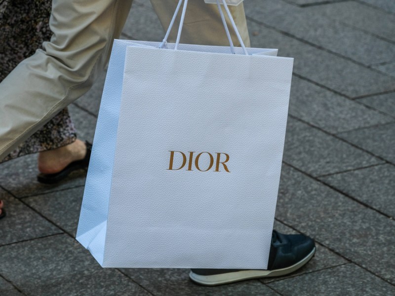 Eine Person trägt eine weiße „Dior“-Tüte.