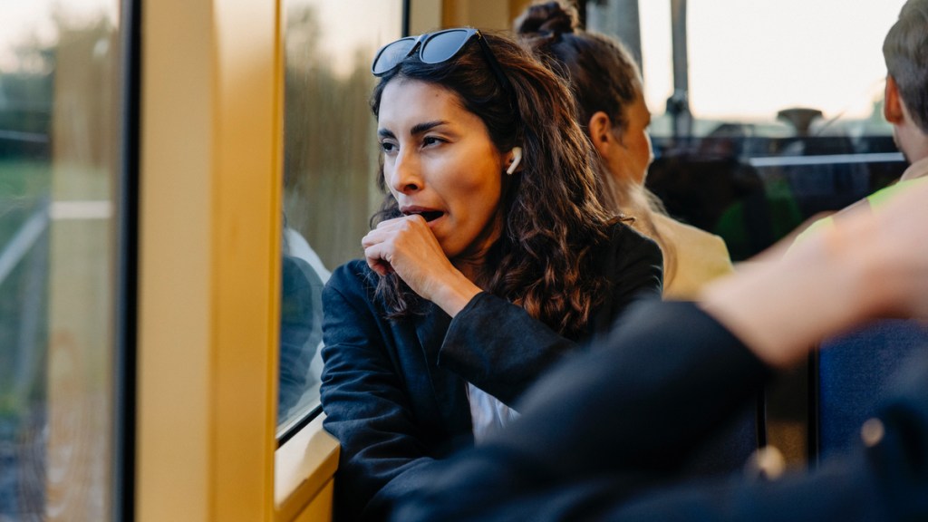 Eine Frau im Bus hält sich die Hand vor den Mund, während die gähnt.