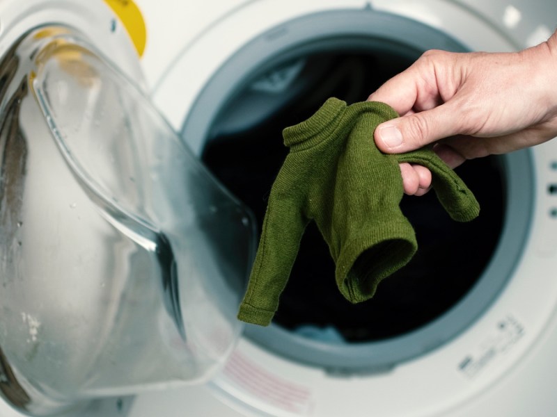 Eine Hand holt einen grünen, eingelaufenen Pulli aus der Waschmaschine.