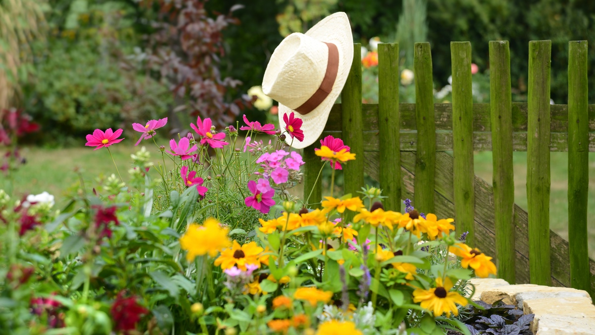 Ein blühender Garten, an dessen Zaun ein weißer Hut hängt.