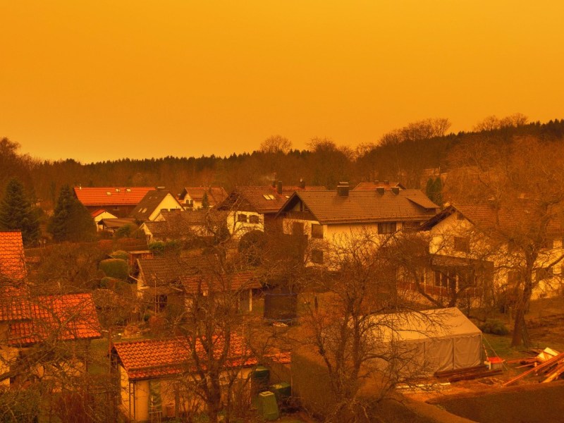 Saharastaub über Gärten und Rasenflächen einer Kleinstadt färbt den Himmel gelb.