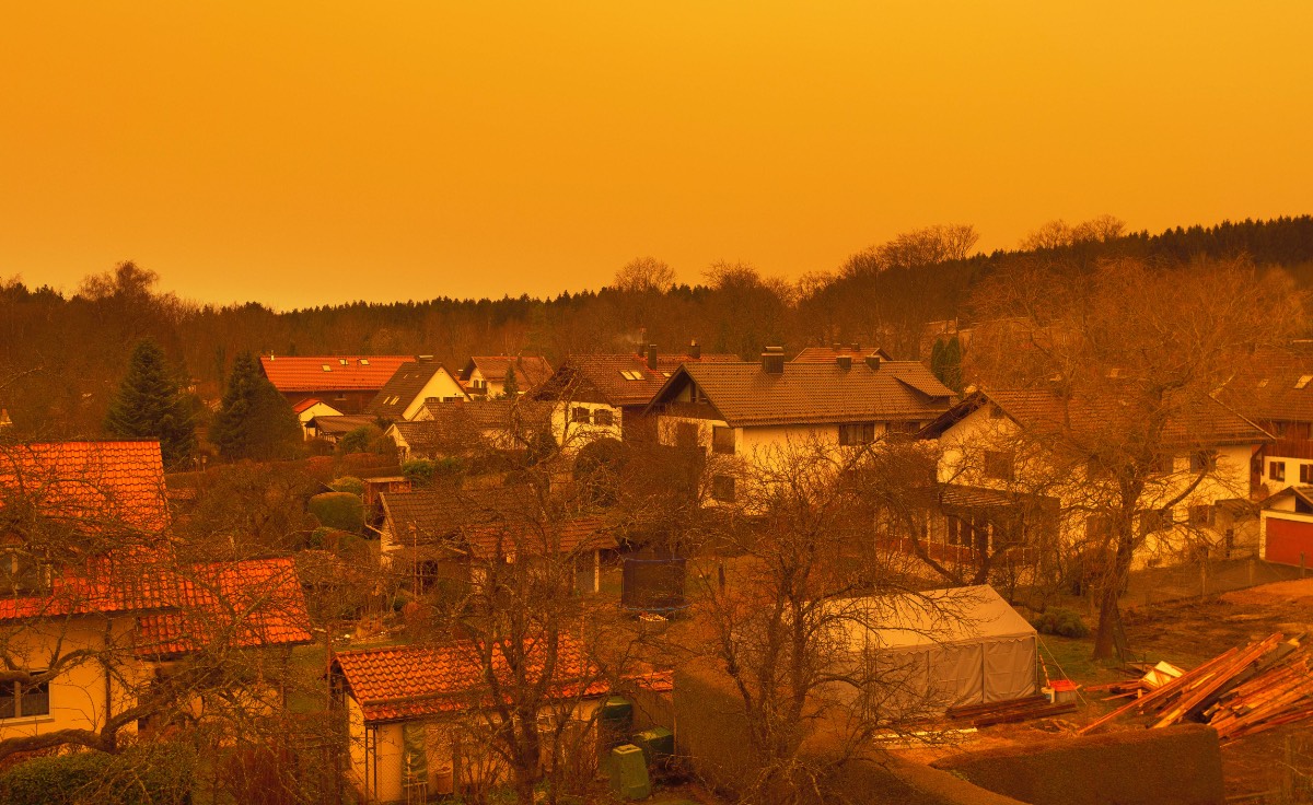 Saharastaub über Gärten und Rasenflächen einer Kleinstadt färbt den Himmel gelb.