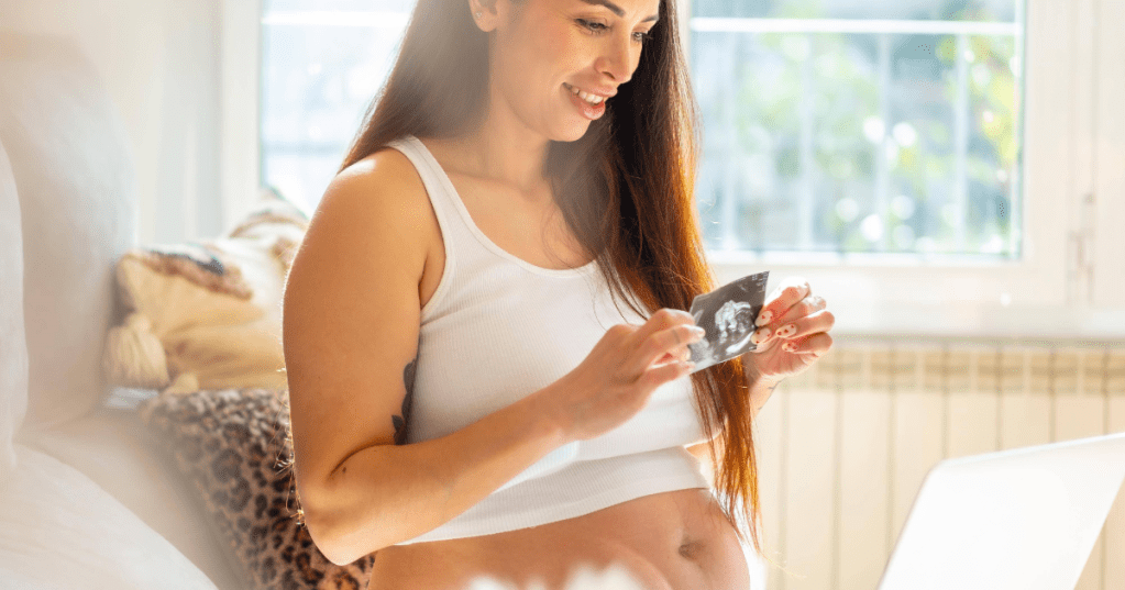 Schwangerschaft und Alter: Junge schwangere Frau hält Ultraschall in eine Kamera.