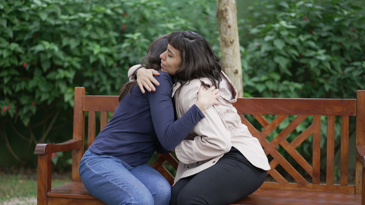 Zwei Frauen auf einer Bank umarmen sich.
