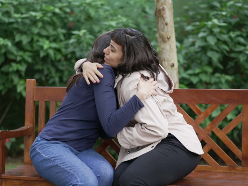 Zwei Frauen auf einer Bank umarmen sich.