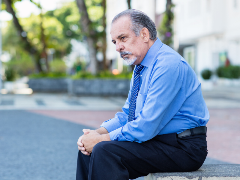 Ein traurig aussehender Mann sitzt auf einer Mauer.