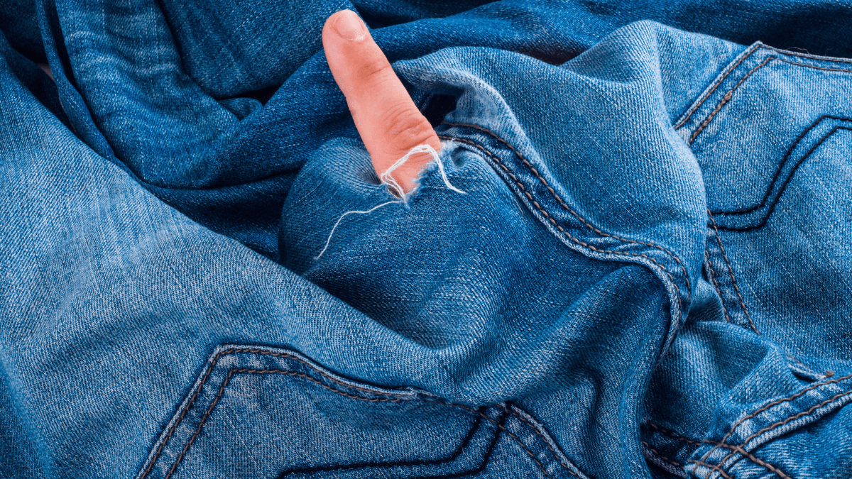 Ein Loch in einer blauen Jeans, durch das jemand einen Finger steckt.