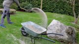 Quarzsand wird mit einer Schaufel auf einem Rasen in einem Garten ausgebracht.