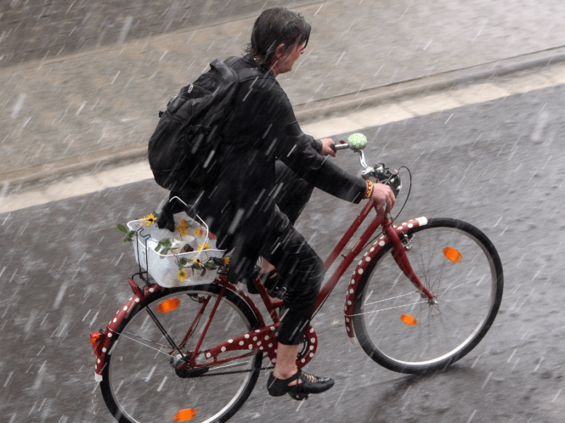 Eine Frau fährt mit ihrem Fahrrad durch den Regen.
