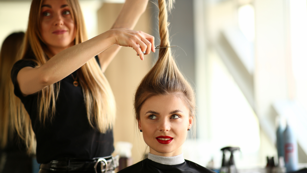 Eine Friseuse hält das Haar ihrer blonden Kundin hoch und hält eine Schere daran.