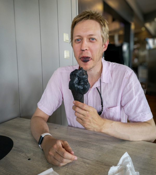 Ein Mann isst ein Lakritzeis und streckt seine Zunge heraus.