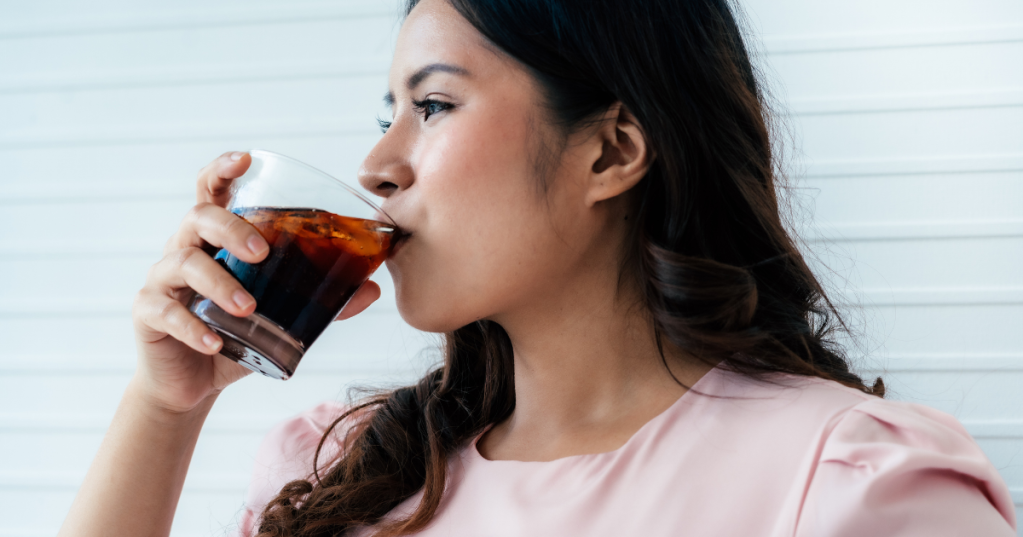 Frau lacht und trinkt ein Glas Cola.