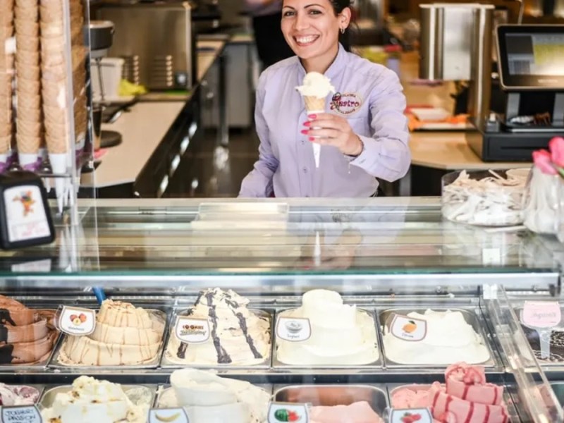 Frau steht hinter einer Theke und verkauft ein Eis in einer Waffel.