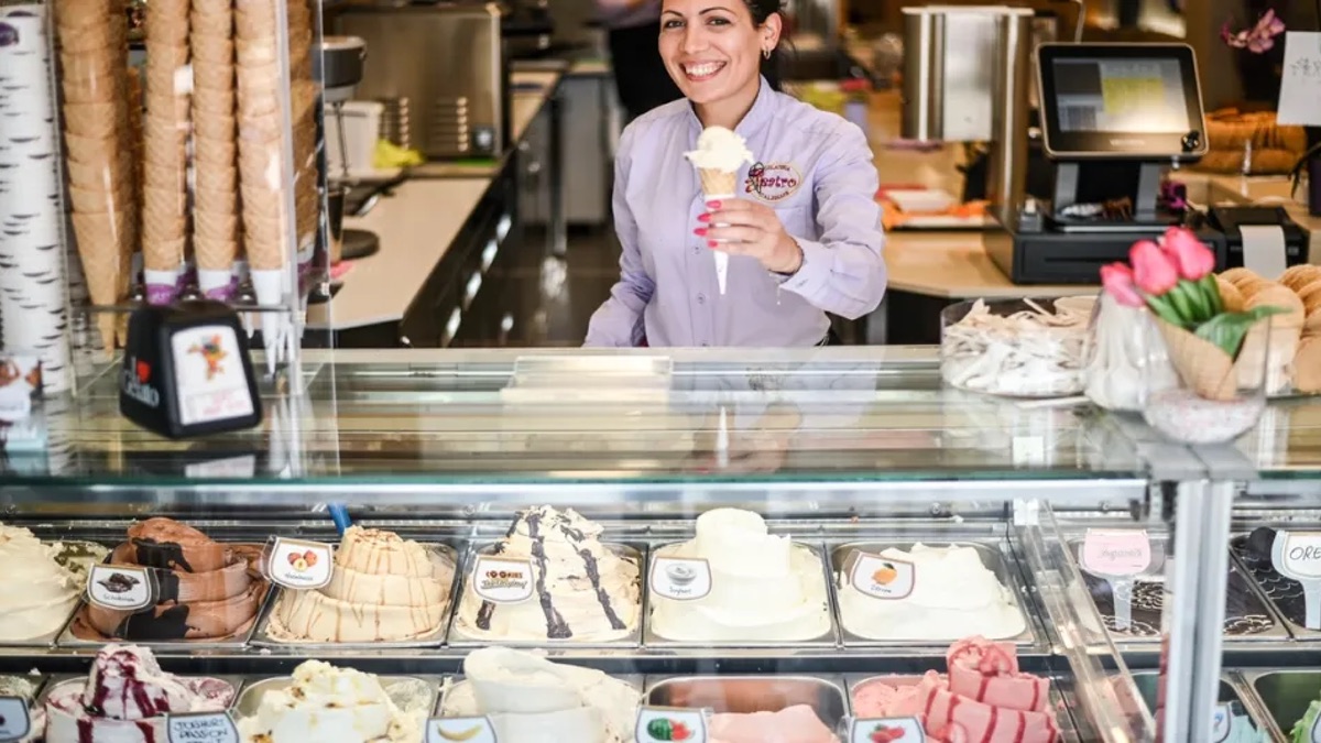 Frau steht hinter einer Theke und verkauft ein Eis in einer Waffel.
