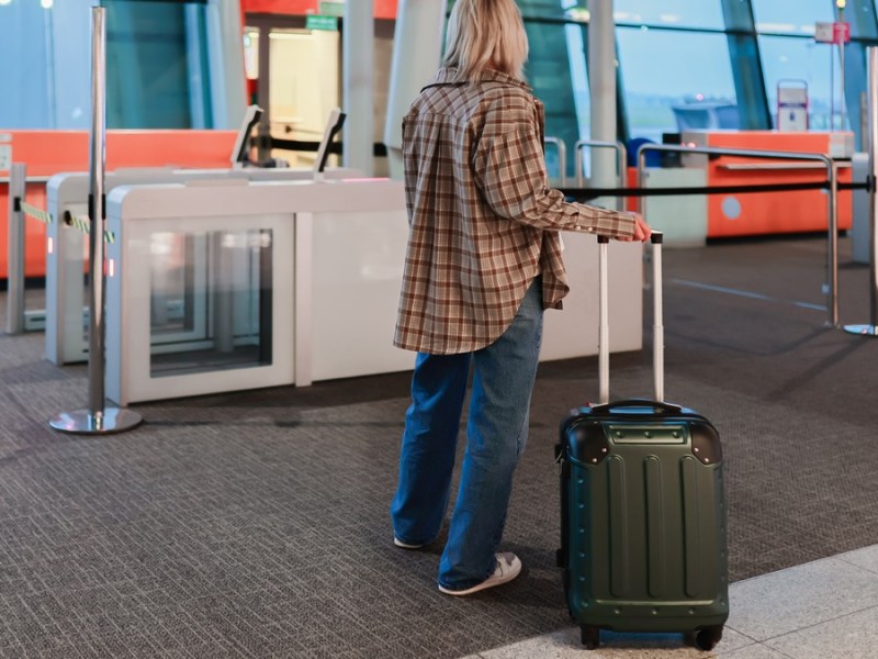 Frau steht mit Koffer am Flughafen.
