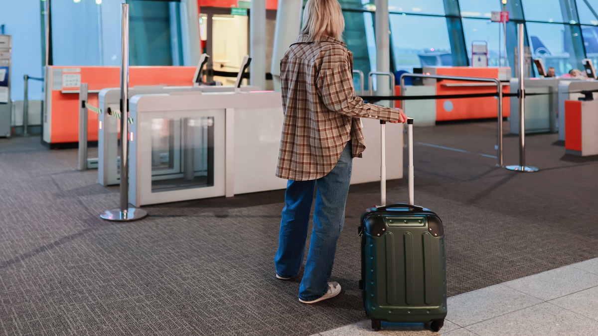 Frau steht mit Koffer am Flughafen.