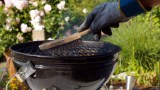 Eine Person reinigt einen Grill mit einer Bürste.
