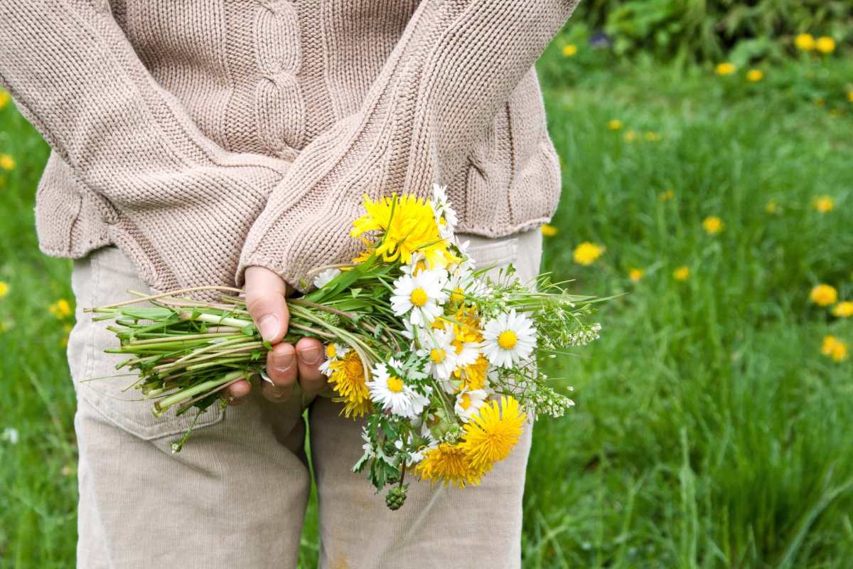 Eine Frau hält einen großen Wildblumenstrauß hinter ihrem Rücken versteckt.