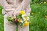 Eine Frau hält einen großen Wildblumenstrauß hinter ihrem Rücken versteckt.