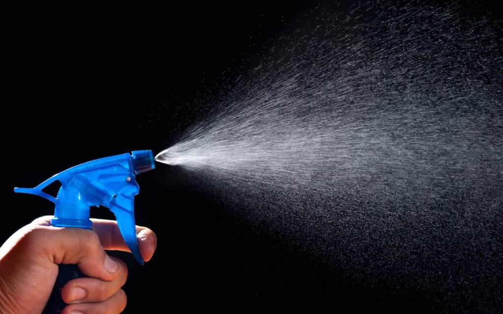 Wasser wird aus einer Sprühflasche gesprüht, Nahaufnahme vor schwarzem Hintergrund.