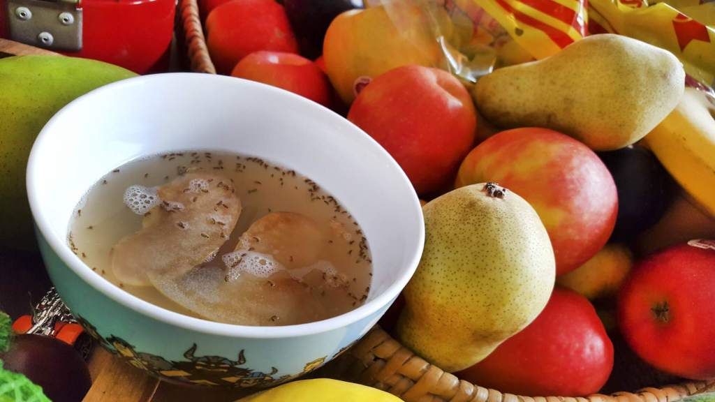 Eine selbstgemachte Fruchtfliegenfalle aus Essig und Spülmittel steht zwischen Obst in einer Küche.
