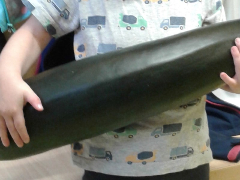 Ein kleines Mädchen hält eine riesige Zucchini im Arm.