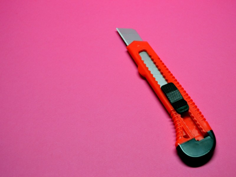Ein rotes Cuttermesser vor einem pinken Hintergrund.