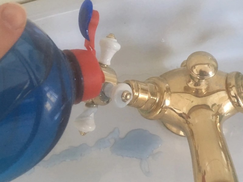 Spülmittel wird auf einen goldenen Wasserhahn gegeben.