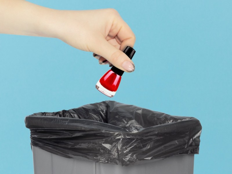 Eine Person wirft ein Nagellackfläschchen in den Mülleimer.