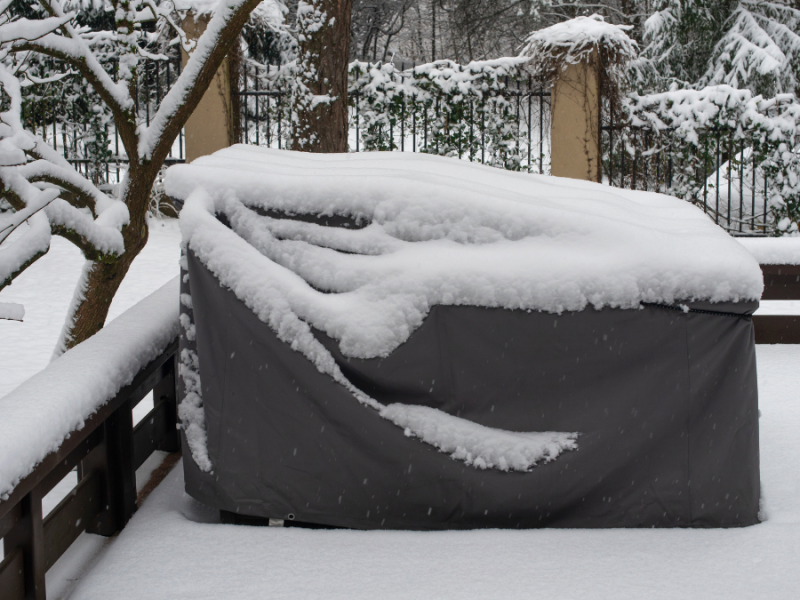 Mit einer Schutzfolie abgedeckte Gartenmöbel, auf denen Schnee liegt.