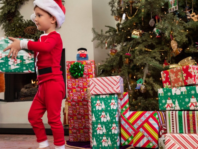 kleiner Junge im Weihnachtskostüm und ein Weihnachtsbaum, unter dem viele Geschenke liegen