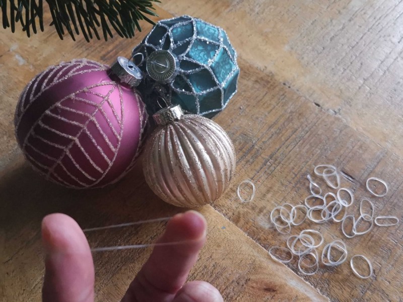 drei Weihnachtskugeln und durchsichtige Gummibänder liegen auf einem Tisch